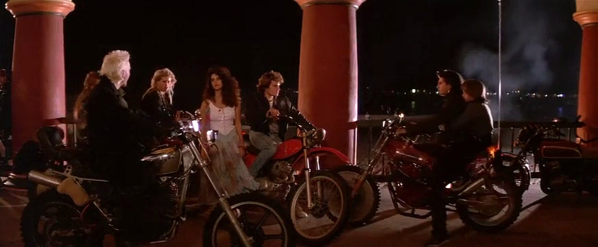Fig. 13:The Lost Boys (1987) henviser til klassiske juvenile delinquent-film, fx The Wild One (1953) med Marlon Brando, og nogle af 1960’ernes og 1970’ernes film om utilpassende men tiltrækkende unge fyre fra ”the wrong side of the tracks”, heriblandt West Side Story (1964), The Wild Angels (1966) og Grease (1978). Bemærk hvordan den unge, flotte pige kigger intenst og interesseret på den vilde David. Det kan nok være at han er farlig, men han er også dragende og tillokkende.